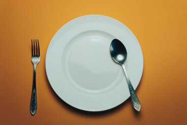 Beyaz kase ve turuncu arka planda kaşıkla çatal.