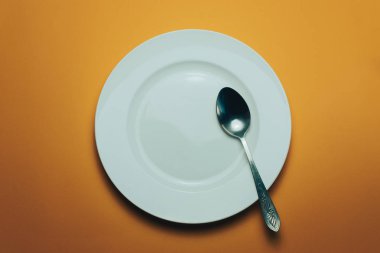 Beyaz kase ve turuncu arka planda kaşıkla çatal.