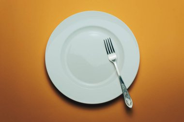 Beyaz kase ve turuncu arka planda kaşıkla çatal.