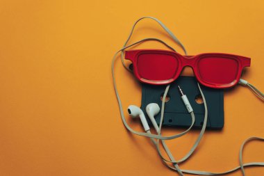 Turuncu arka planda kırmızı camlı, siyah manyetik kaset ve beyaz kulaklıklar.