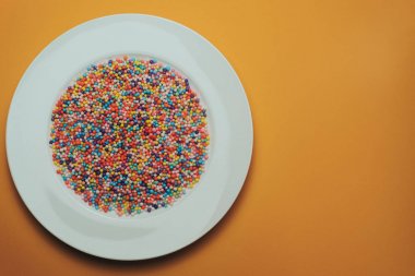 Turuncu bir zemin üzerinde renkli hazırlanmış beyaz tabak (vitaminler, boyalar, lezzet artırıcılar, beslenme takviyeleri, yenilikçi teknolojiler, şeker tatlılar).