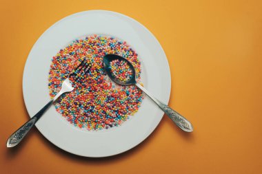 Turuncu bir zemin üzerinde renkli hazırlanmış beyaz tabak (vitaminler, boyalar, lezzet artırıcılar, beslenme takviyeleri, yenilikçi teknolojiler, şeker tatlılar).