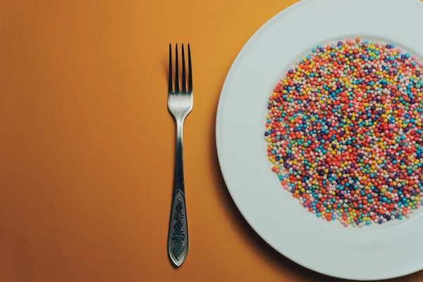 Turuncu bir zemin üzerinde renkli hazırlanmış beyaz tabak (vitaminler, boyalar, lezzet artırıcılar, beslenme takviyeleri, yenilikçi teknolojiler, şeker tatlılar).