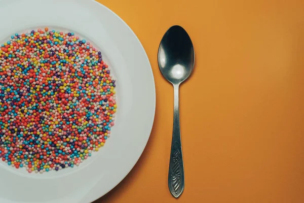 White plate with color preparations (vitamins, dyes, flavor enhancers, nutritional supplements, innovative technologies, candy sweets) on an orange background.