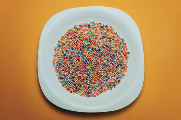 White plate with color preparations (vitamins, dyes, flavor enhancers, nutritional supplements, innovative technologies, candy sweets) on an orange background.