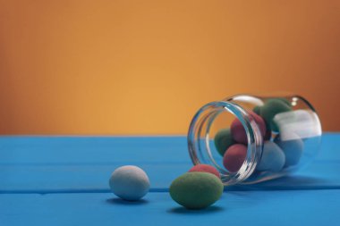 Çikolata ve krema içinde çok renkli fıstık küçük bir şişe. Mavi ahşap masa ve sarı arka plan. Makro görünümü.