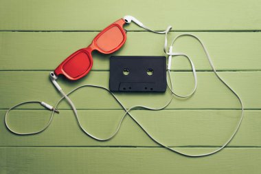 Yeşil ahşap masa arka plan üzerinde kırmızı camlı, siyah manyetik kaset ve beyaz kulaklıklar.