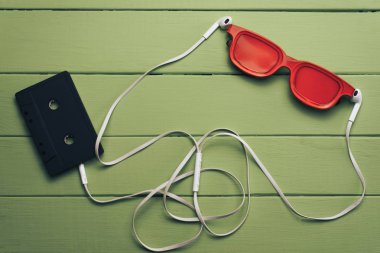 Yeşil ahşap masa arka plan üzerinde kırmızı camlı, siyah manyetik kaset ve beyaz kulaklıklar.