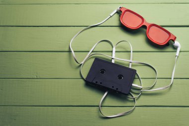 Yeşil ahşap masa arka plan üzerinde kırmızı camlı, siyah manyetik kaset ve beyaz kulaklıklar.