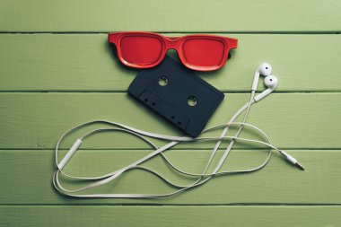 Yeşil ahşap masa arka plan üzerinde kırmızı camlı, siyah manyetik kaset ve beyaz kulaklıklar.