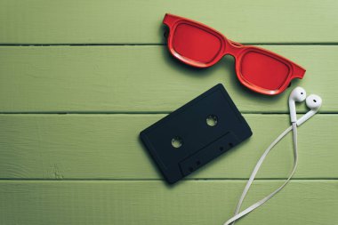 Yeşil ahşap masa arka plan üzerinde kırmızı camlı, siyah manyetik kaset ve beyaz kulaklıklar.