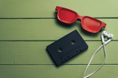 Yeşil ahşap masa arka plan üzerinde kırmızı camlı, siyah manyetik kaset ve beyaz kulaklıklar.