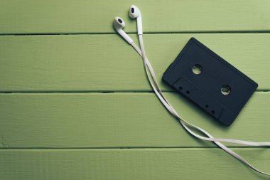 Yeşil ahşap masa arka planında siyah manyetik kaset ve beyaz kulaklıklar.