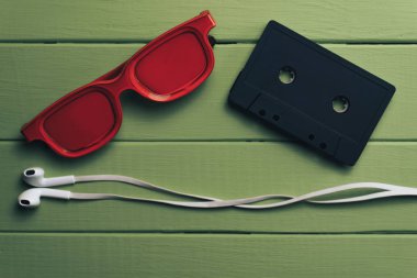 Yeşil ahşap masa arka plan üzerinde kırmızı camlı, siyah manyetik kaset ve beyaz kulaklıklar.