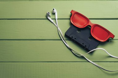 Yeşil ahşap masa arka planında siyah manyetik kaset ve beyaz kulaklıklar.