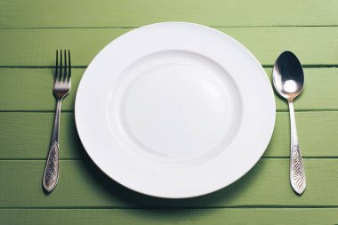 Beyaz tabak ve çatal ile yeşil tahta masa üzerinde kaşık..