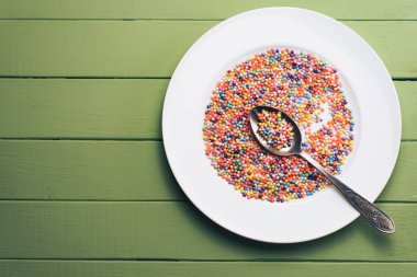 Renk hazırlı beyaz tabak (vitaminler, boyalar, lezzet artırıcılar, besin takviyeleri, yenilikçi teknolojiler, şeker tatlılar) yeşil tahta masa arka planında.