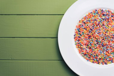 Renk hazırlı beyaz tabak (vitaminler, boyalar, lezzet artırıcılar, besin takviyeleri, yenilikçi teknolojiler, şeker tatlılar) yeşil tahta masa arka planında.
