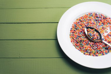 Renk hazırlı beyaz tabak (vitaminler, boyalar, lezzet artırıcılar, besin takviyeleri, yenilikçi teknolojiler, şeker tatlılar) yeşil tahta masa arka planında.
