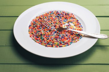 Renk hazırlı beyaz tabak (vitaminler, boyalar, lezzet artırıcılar, besin takviyeleri, yenilikçi teknolojiler, şeker tatlılar) yeşil tahta masa arka planında.