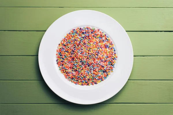 White plate with color preparations (vitamins, dyes, flavor enhancers, nutritional supplements, innovative technologies, candy sweets) on an green wooden table background.