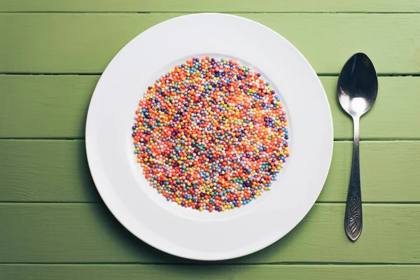 White plate with color preparations (vitamins, dyes, flavor enhancers, nutritional supplements, innovative technologies, candy sweets) on an green wooden table background.