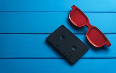 Kırmızı gözlük, mavi ahşap masa arka plan üzerinde klasik manyetik kaset.