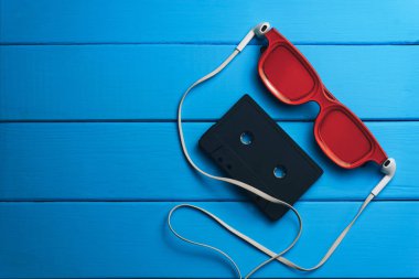 Kırmızı gözlük, klasik manyetik kaset ve mavi ahşap masa arka plan üzerinde beyaz kulaklıklar.