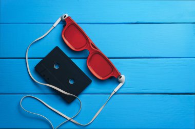 Kırmızı gözlük, klasik manyetik kaset ve mavi ahşap masa arka plan üzerinde beyaz kulaklıklar.