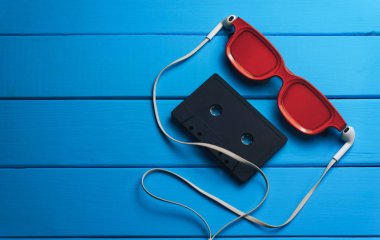 Kırmızı gözlük, klasik manyetik kaset ve mavi ahşap masa arka plan üzerinde beyaz kulaklıklar.