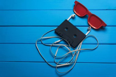 Kırmızı gözlük, klasik manyetik kaset ve mavi ahşap masa arka plan üzerinde beyaz kulaklıklar.