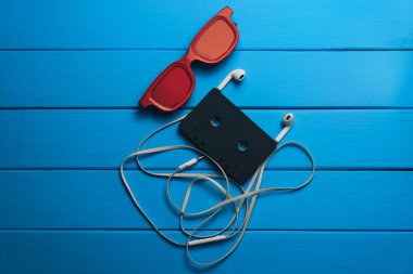 Kırmızı gözlük, klasik manyetik kaset ve mavi ahşap masa arka plan üzerinde beyaz kulaklıklar.