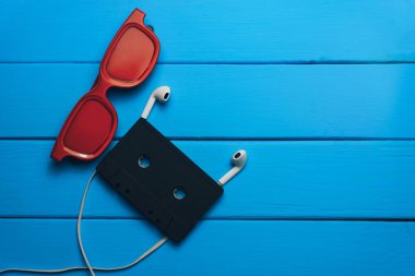 Kırmızı gözlük, klasik manyetik kaset ve mavi ahşap masa arka plan üzerinde beyaz kulaklıklar.