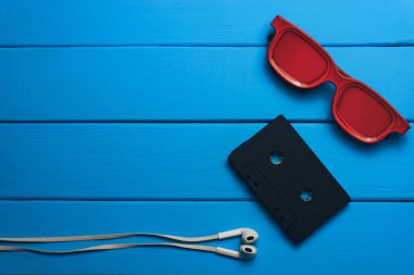 Kırmızı gözlük, klasik manyetik kaset ve mavi ahşap masa arka plan üzerinde beyaz kulaklıklar.