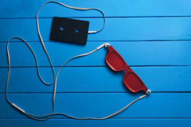 Kırmızı gözlük, klasik manyetik kaset ve mavi ahşap masa arka plan üzerinde beyaz kulaklıklar.