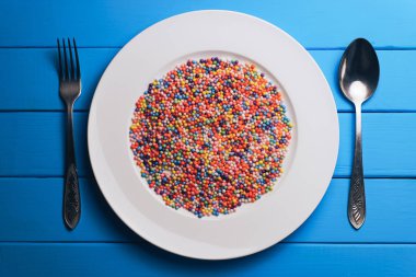 Mavi ahşap masa arkaplanında beyaz tabak (vitaminler, boyalar, lezzet artırıcılar, beslenme takviyeleri, yenilikçi teknolojiler, şekerleme tatlılar)..