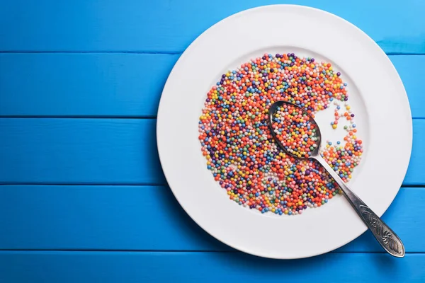 White plate with color preparations (vitamins, dyes, flavor enhancers, nutritional supplements, innovative technologies, candy sweets) on an blue wooden table background.