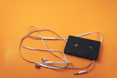 Turuncu arka planda siyah klasik manyetik kaset ve beyaz kulaklıklar.