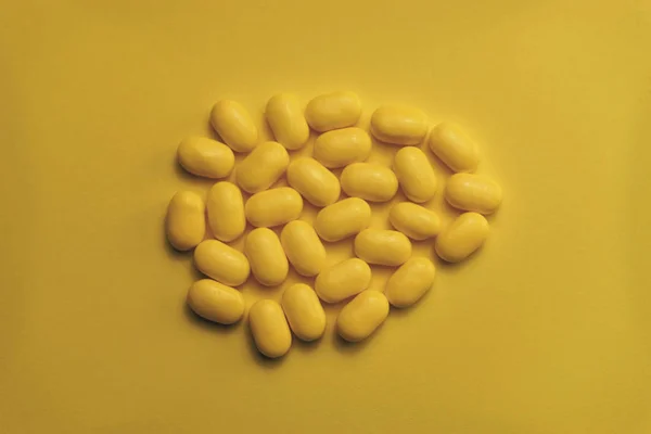 Yellow pills on a yellow table background.