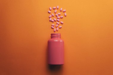 Turuncu bir arka plan üzerinde güzel pembe şişe ve pembe haplar. Üstte görüntü.