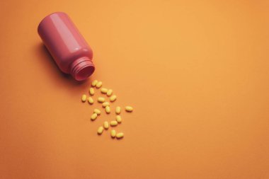 Turuncu bir arka plan üzerinde güzel pembe şişe ve sarı haplar. Üstte görüntü.