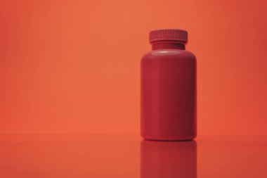 Bir cam masa ve mercan turuncu arka plan üzerinde haplar için pembe şişe.