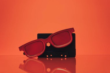 Siyah klasik manyetik kaset ve cam bir masa üzerinde kırmızı gözlük. Güzel mercan turuncu arka plan.