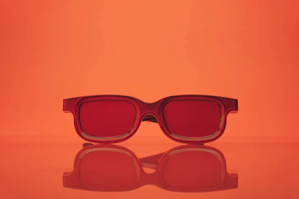 Red glasses on a glass table and coral orange background. Summer concept.