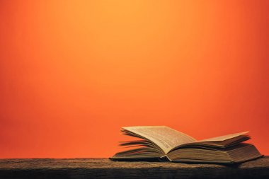 Eski bir meşe ahşap masa ve mercan turuncu duvar arka plan arkasında eski kitap.