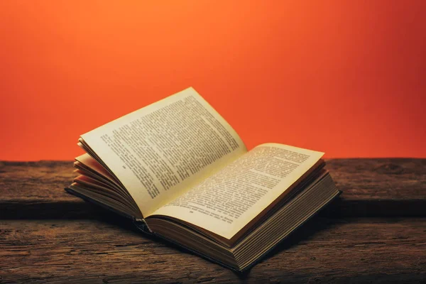 Eski bir meşe ahşap masa ve mercan turuncu duvar arka plan arkasında eski kitap.