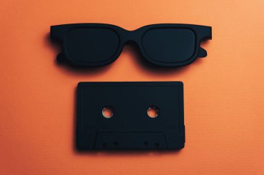 Güzel bir mercan turuncu arka plan üzerinde siyah klasik manyetik kaset ve siyah gözlük.