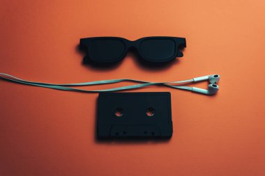 Siyah gözlük, siyah manyetik kaset ve beyaz kulaklıklar güzel bir mercan turuncu arka plan.