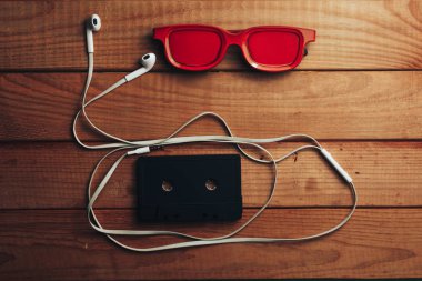 Kırmızı gözlük, klasik manyetik kaset ve kahverengi ahşap masa arka plan üzerinde beyaz kulaklıklar.