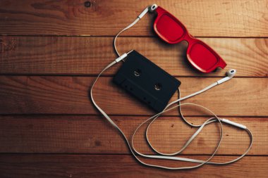 Kırmızı gözlük, klasik manyetik kaset ve kahverengi ahşap masa arka plan üzerinde beyaz kulaklıklar.